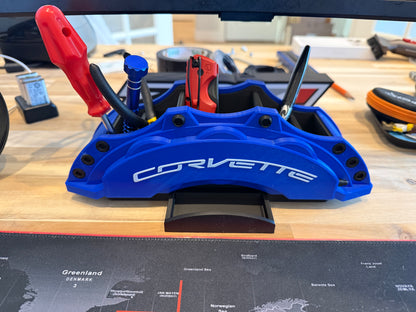 Blue Corvette brake caliper on a workbench with tools in the background